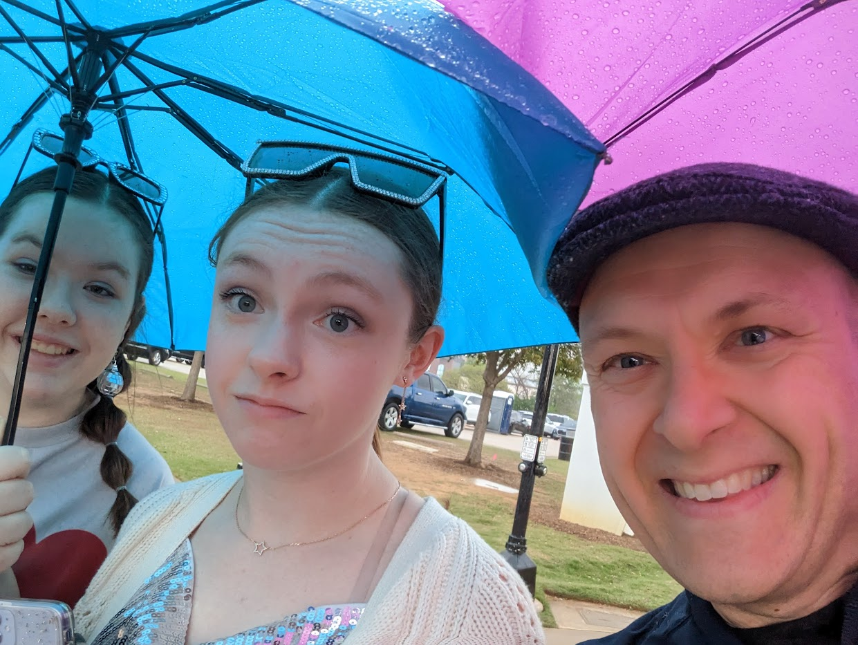 Andrew and his daughters under umbrellas heading into The Eras Tour.